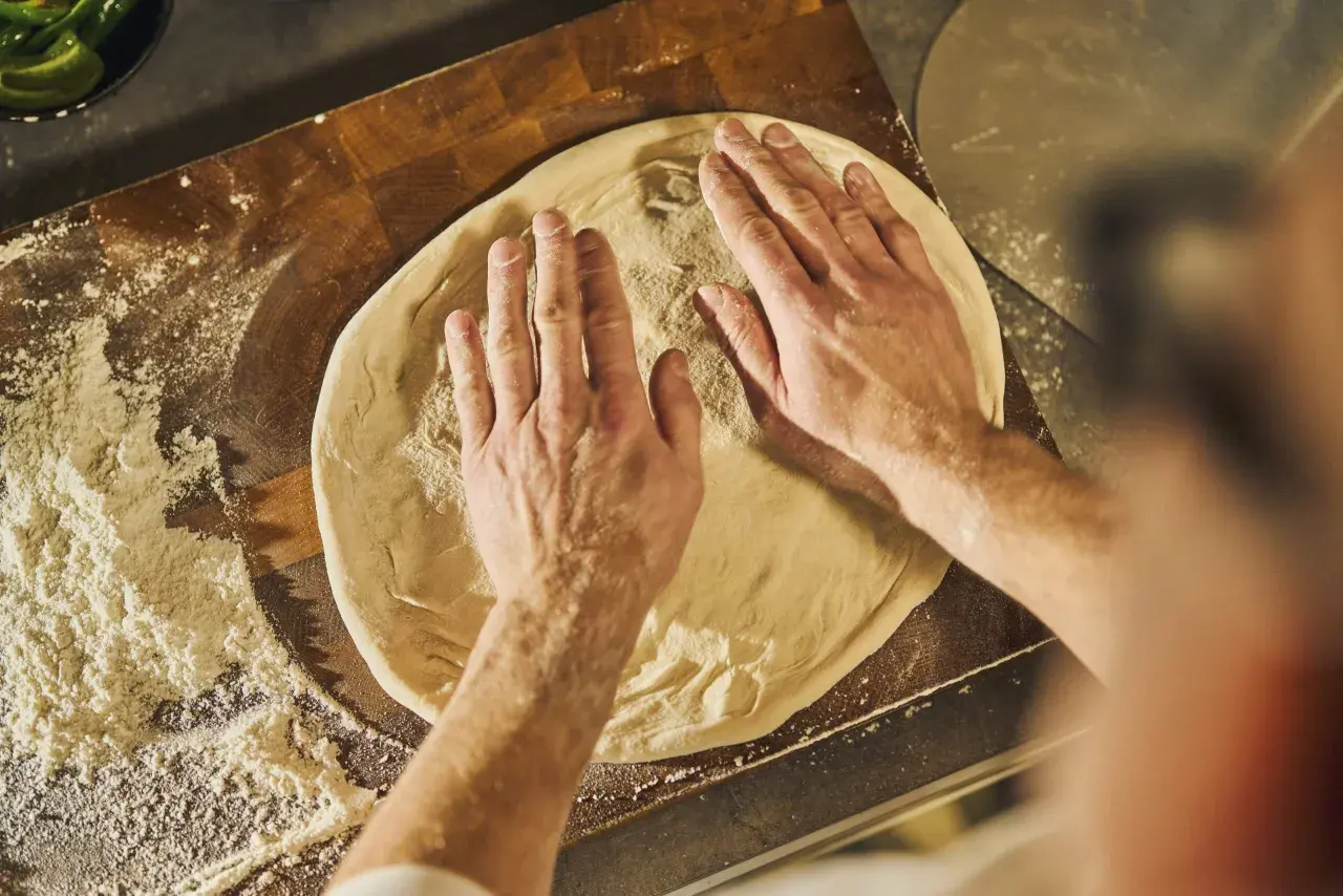 Händer formar pizzadeg på en skärbräda med mjöl. Ett steg i ett klassiskt pizza recept.