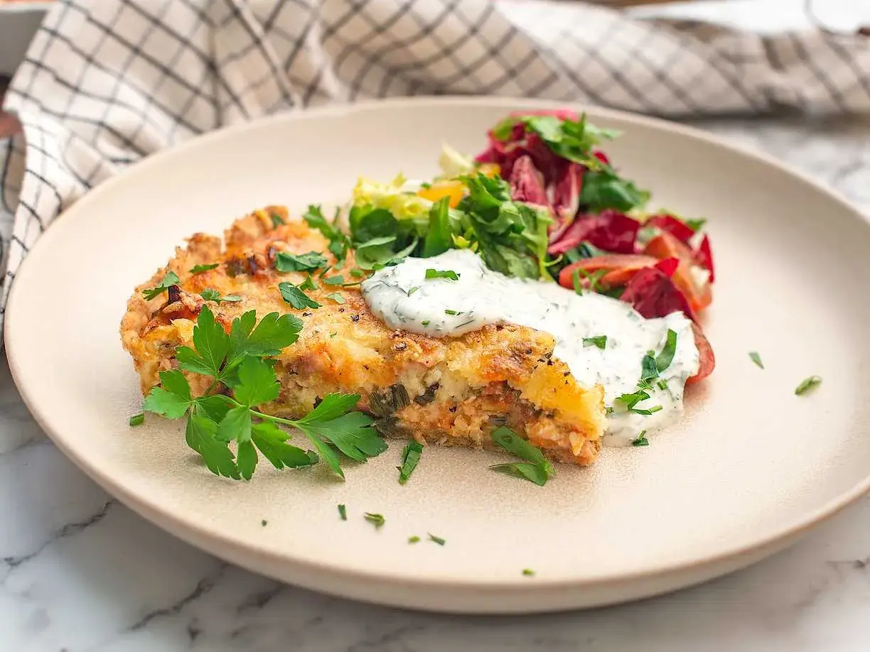 En bit saftig skinkpaj utan ost, toppad med färska örter och en klick krämig sås, serveras med en fräsch sallad.