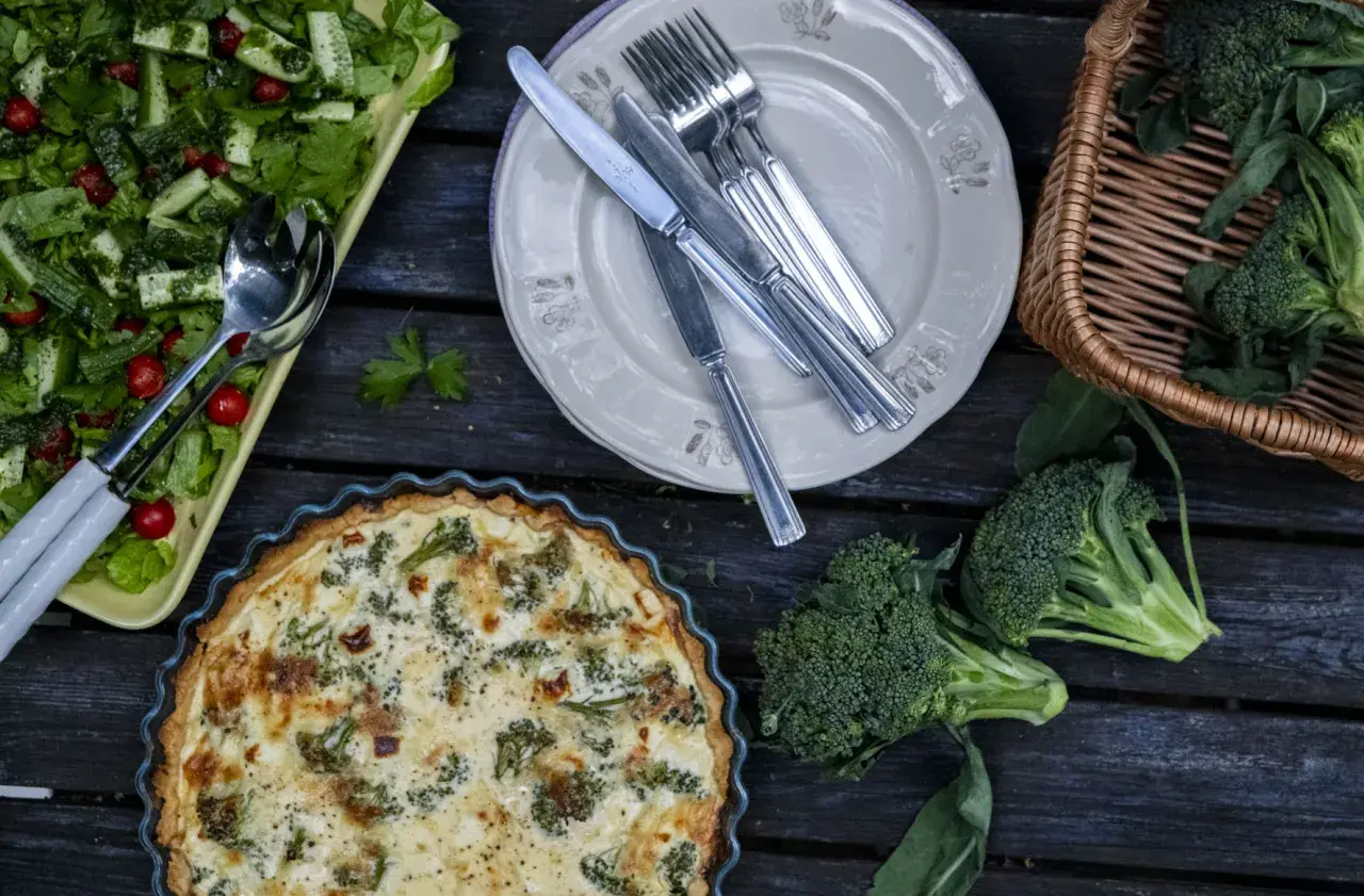 En gyllene västerbottenpaj med broccoli, en fräsch sallad och färsk broccoli i en korg. En härlig måltid!
