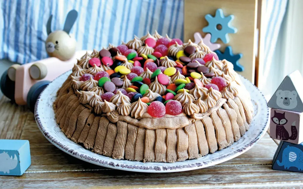 En härlig glutenfri tårta dekorerad med chokladfrosting och färgglada godisar, perfekt för barnkalas.