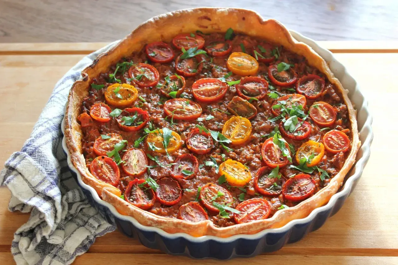 En gyllene köttfärspaj med körsbärstomater och färska örter, redo att serveras.