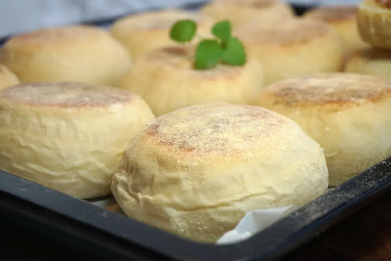 En bricka med nybakade, gyllene english muffins, redo att delas och njutas. En liten grön kvist vilar på en av dem.
