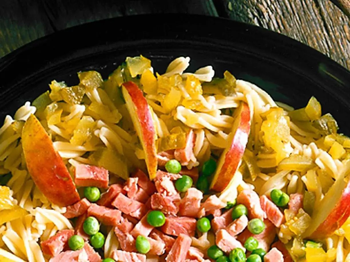 En närbild på en läcker pastasallad med skinka, äppelklyftor och gröna ärtor. En perfekt sommarmåltid!