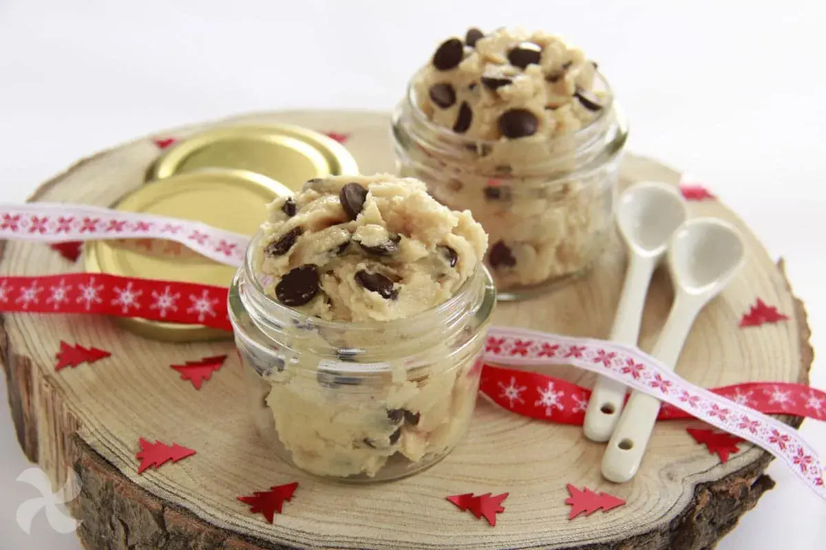 Två glasburkar fyllda med ljuvlig cookie dough, perfekt för ett enkelt cookie dough recept. Julpynt och små skedar ligger redo.