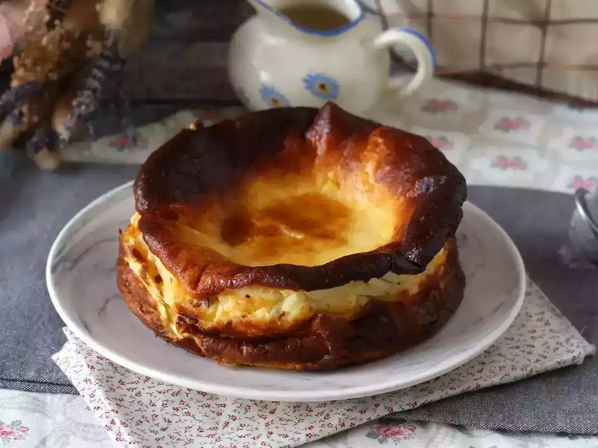 En krämig baskisk cheesecake med karamelliserad yta, serverad på en tallrik med blommig duk.