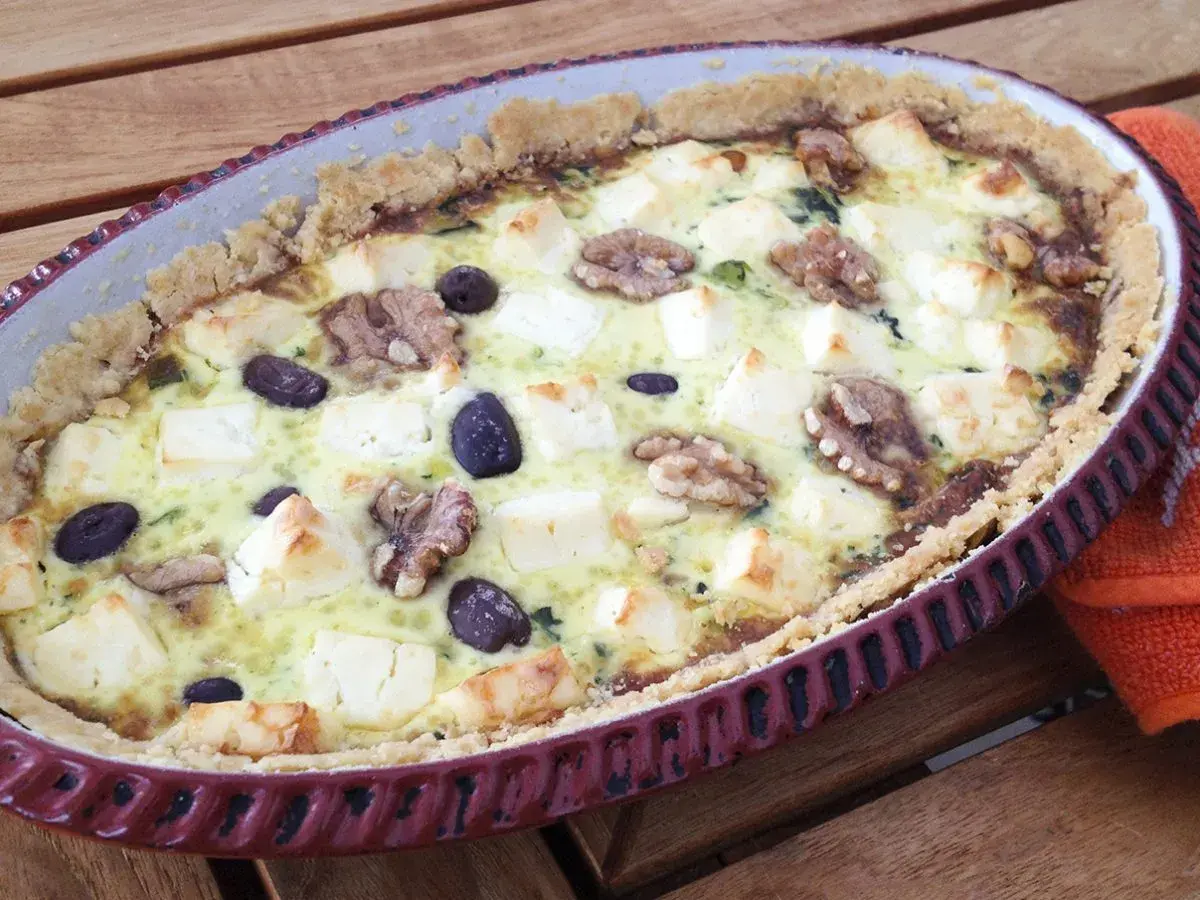 Spinach and feta quiche with walnuts and olives in a rustic tart dish.