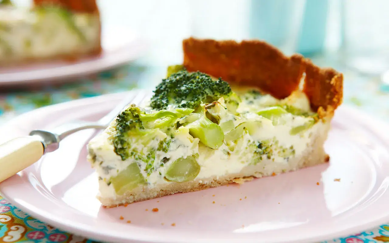 En bit broccoli och ädelostpaj på en rosa tallrik. Pajen har en gyllene botten och fyllning med broccoli och krämig ost.