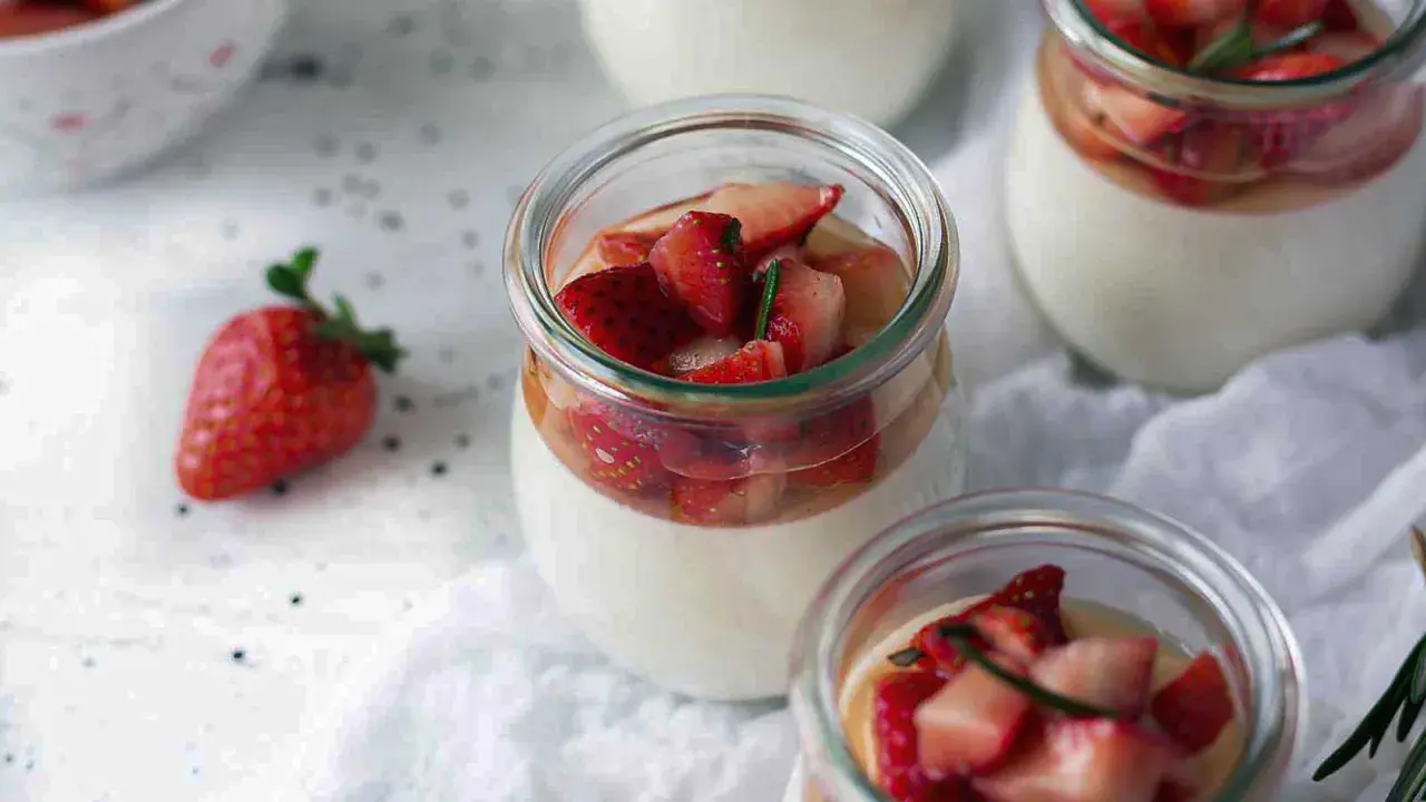 Pannacotta in glass jars topped with fresh strawberries and rosemary.