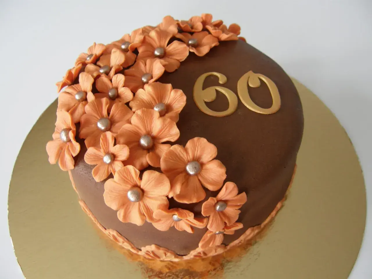 Chokladtårta med aprikosfärgade blommor och guldigt "60" som firar en 60-årig födelsedag.
