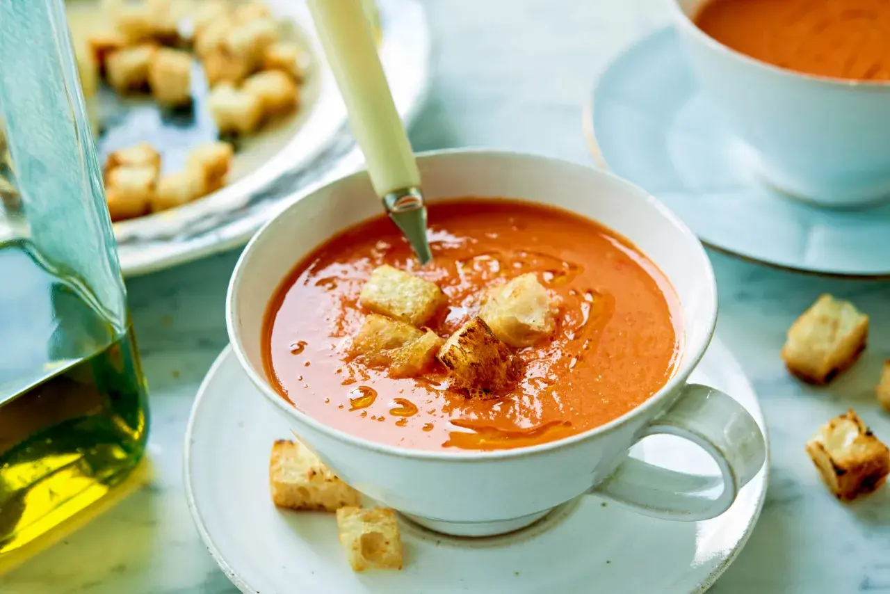 En skål med gazpacho, toppad med krutonger. Bredvid en karaff med olivolja. Ett perfekt gazpacho recept för en varm dag.
