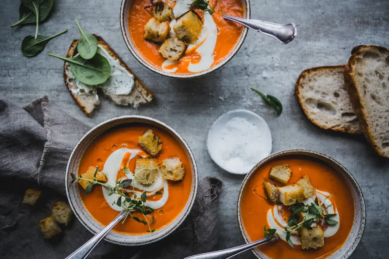 Tre skålar med krämig tomatsoppa, gjord på krossade tomater, toppas med krutonger och en virvel av grädde. Serveras med gott bröd och färsk spenat.