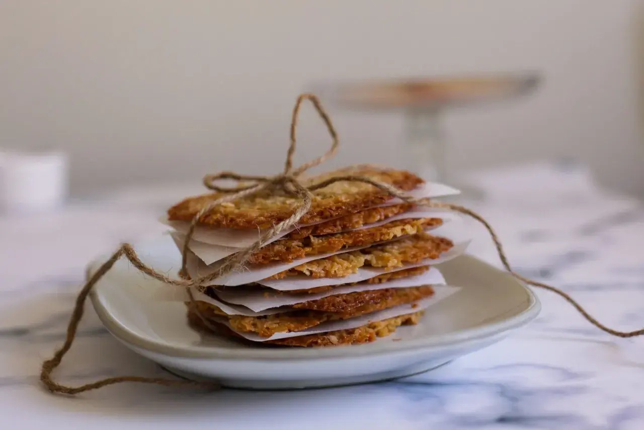 Stack of thin, golden-brown oat cookies tied with twine on a white plate.