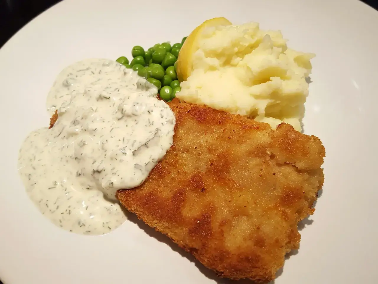 Panerad fisk med potatismos, gröna ärtor och en krämig kall sås till fisk.