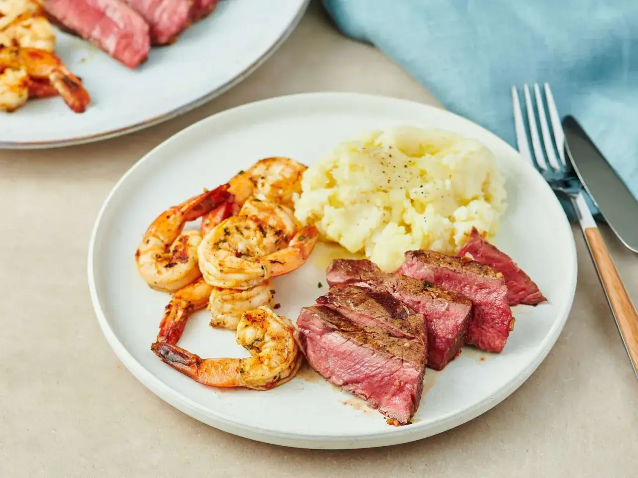 En tallrik med saftigt surf and turf: grillade räkor, skivad biff och krämigt potatismos.