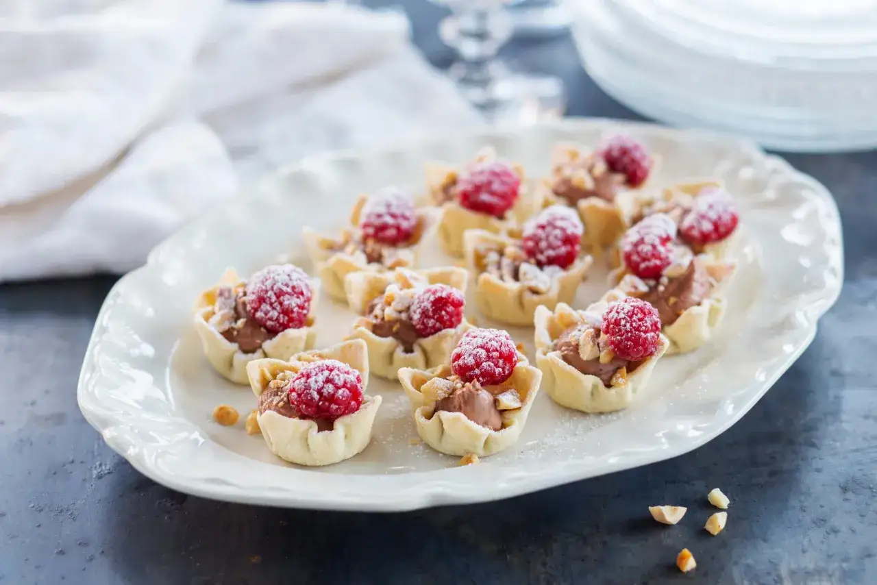 Små krustader i ugn fyllda med chokladkräm, toppade med hallon och strössel. En festlig dessert!