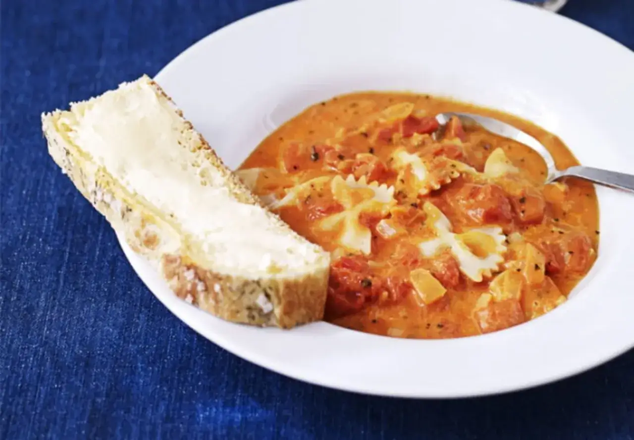 En krämig tomatsoppa med fjärilspasta, perfekt för ett snabbt tomatsoppa recept. Serveras med en skiva smörgås.