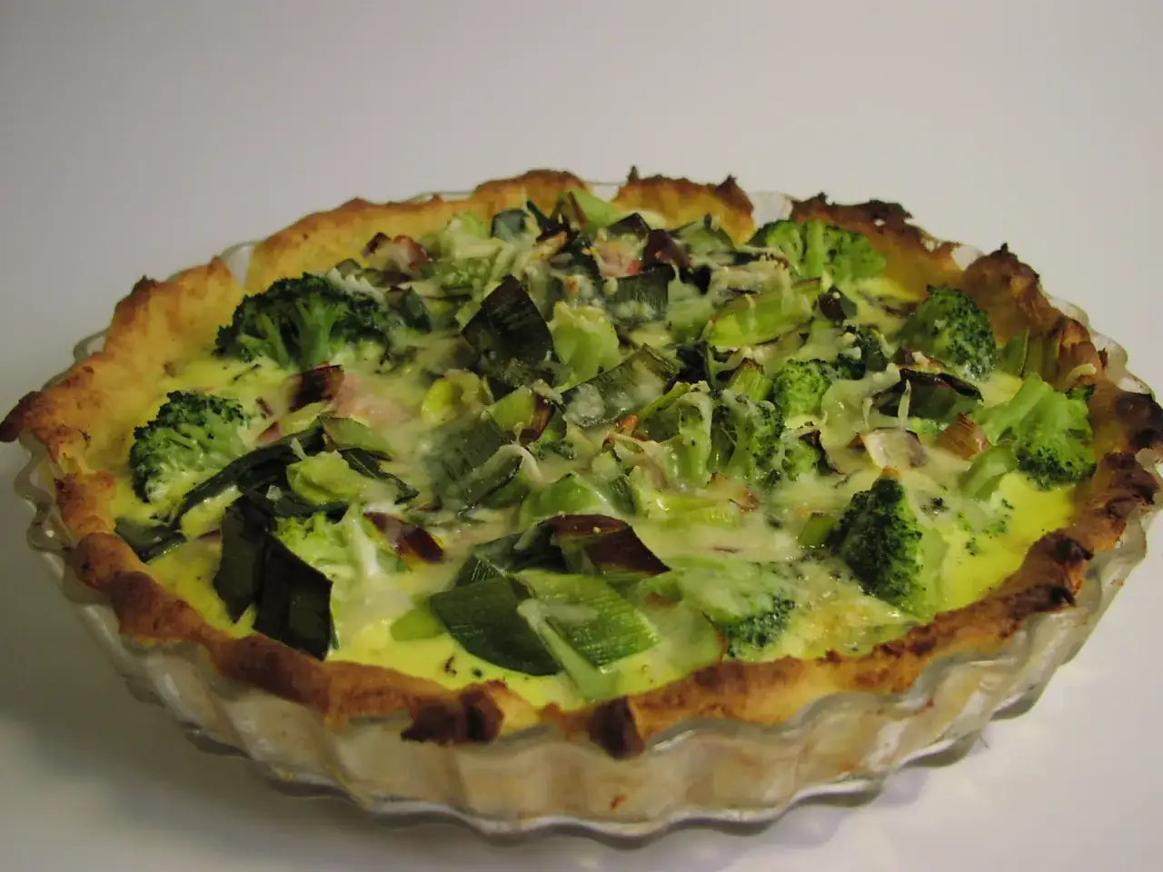 En gyllene broccoli och ädelostpaj med en krispig botten, fylld med gröna broccolibuketter och purjolök i en krämig ädelostsås.