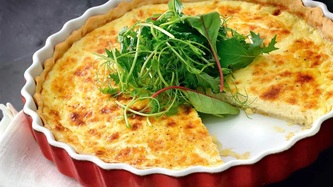 En gyllene ostpaj med olika ostar, toppad med färska gröna blad. Perfekt för en mysig fika.