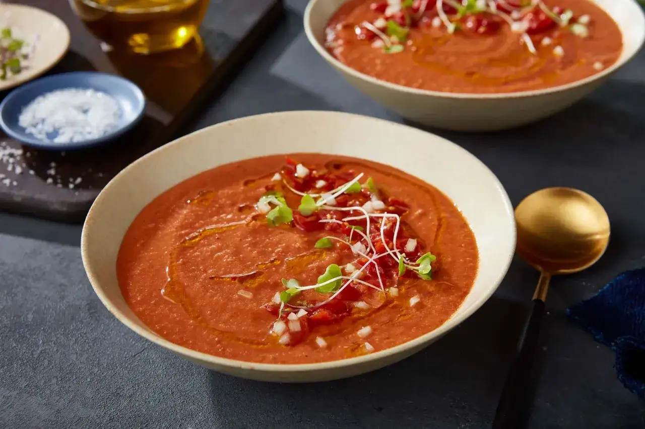 Krämig tomatsoppa med krossade tomater, toppad med färska grönsaker och olivolja. En gyllene sked ligger bredvid.