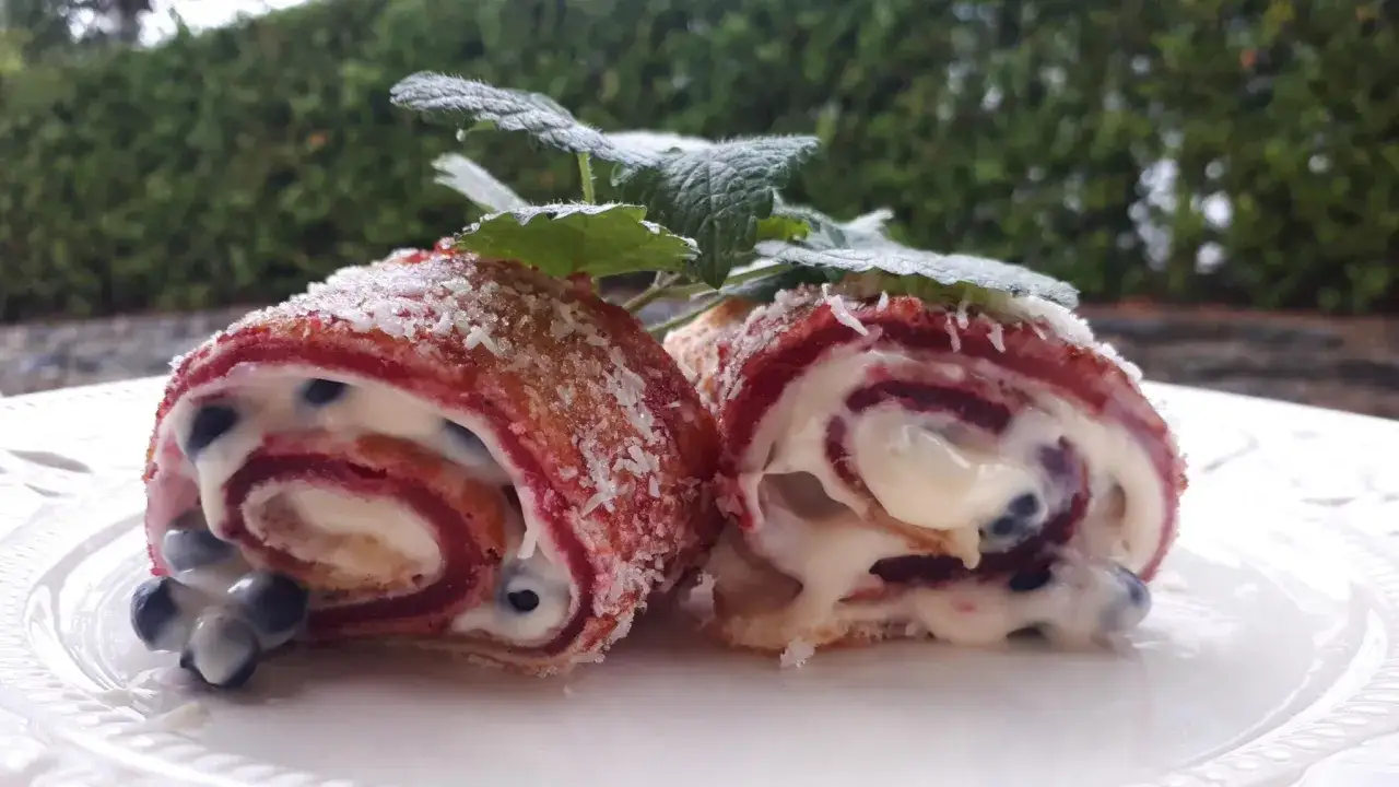 Två bitar av en rulltårta med blåbär och grädde, strödd med kokosflingor. Ett perfekt rulltårta recept för Fredriks fika.