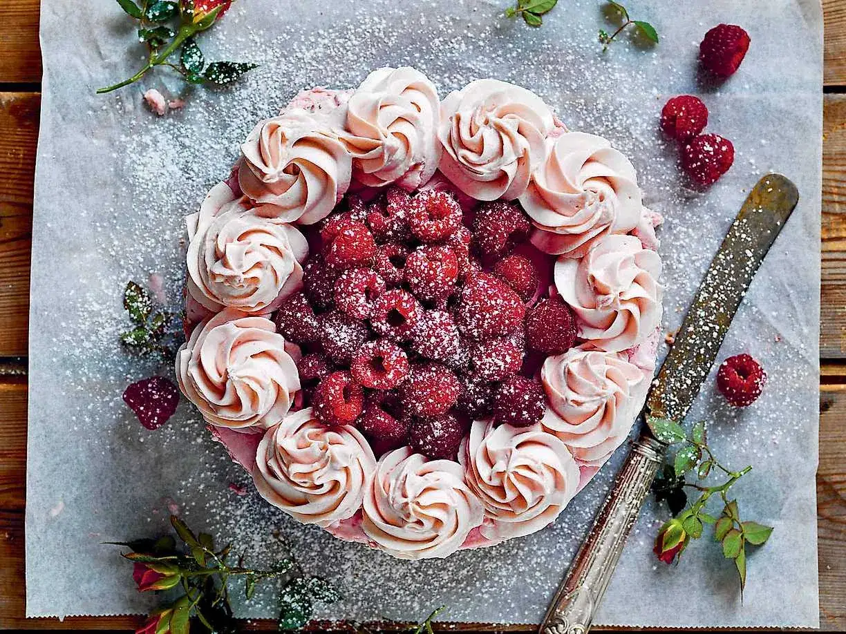 En vacker vit choklad tårta dekorerad med rosa frosting och färska hallon, pudrad med florsocker.