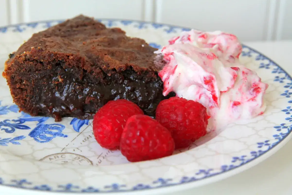 En bit kladdkaka med lakrits, serverad med vispad gr&auml;dde och hallon.