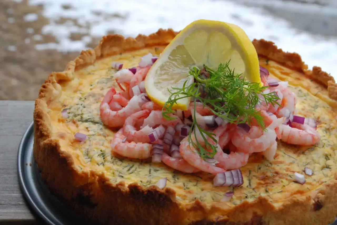 En gyllene räkpaj med dill, toppad med räkor, rödlök, citron och dillkvist. Perfekt för en festlig måltid.