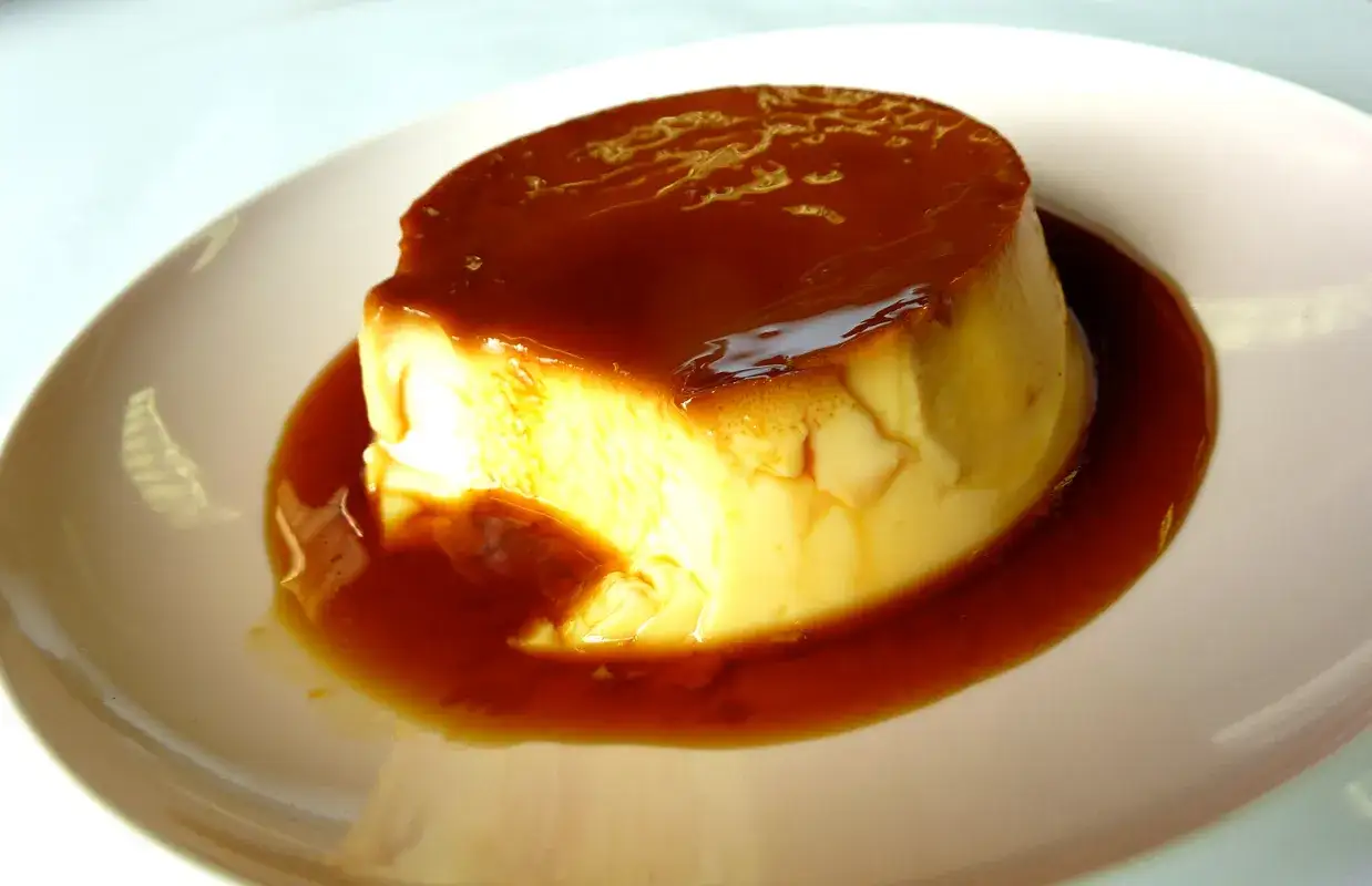 En krämig creme brulee med karamellsås på en vit tallrik.