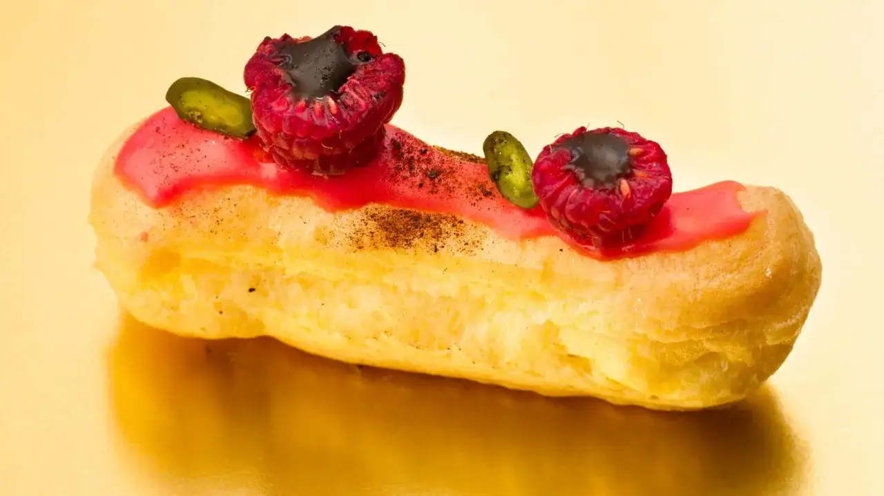 En läcker petit choux med rosa glasyr, hallon och pistagenötter.