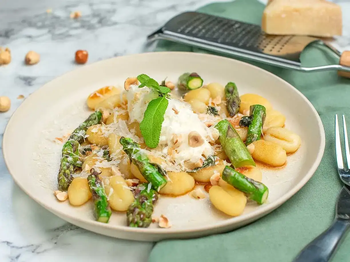 En tallrik med gnocchi, sparris och en klick ricotta, toppad med nötter och parmesan. Ett härligt gnocchi recept för en snabb middag.