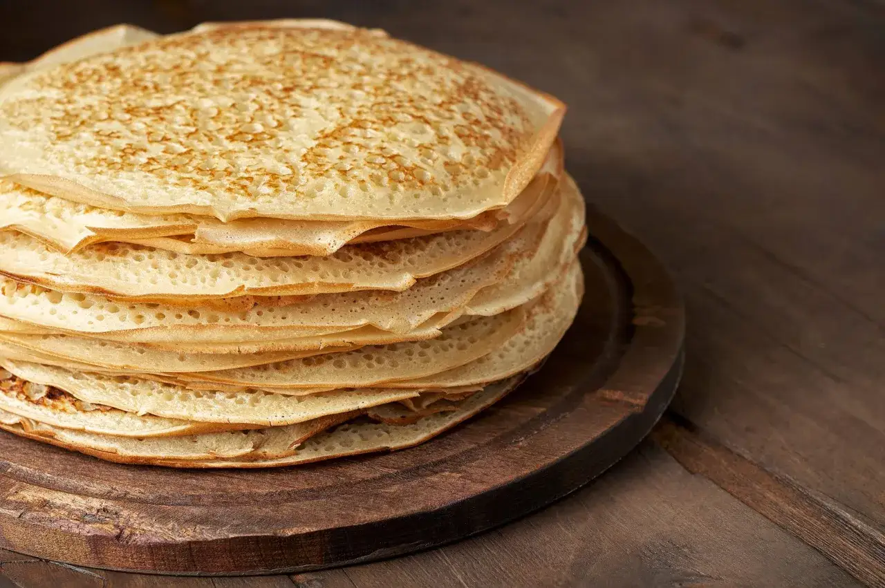 En hög med gyllene pannkakor, perfekt för ett gott pannkakssmet recept. De ligger på en mörk träskärbräda.