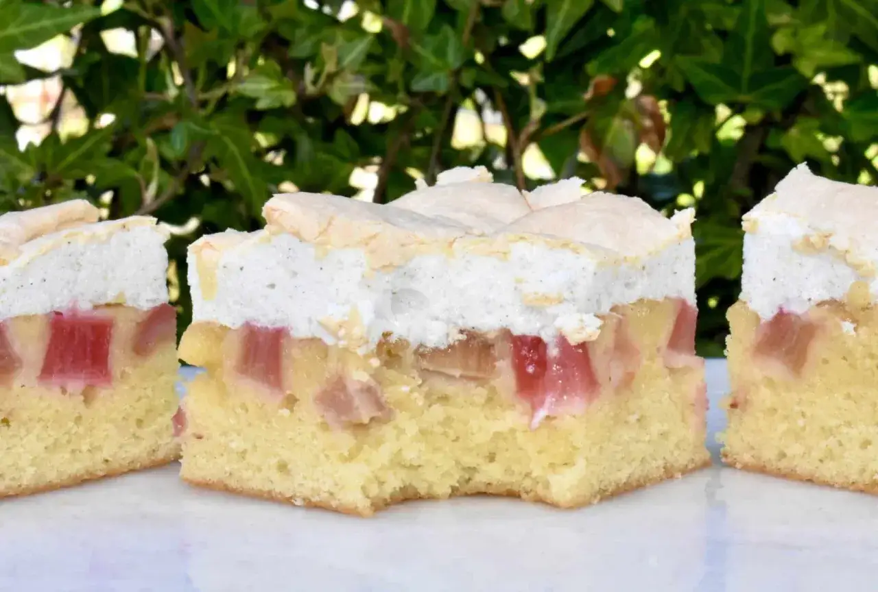Three slices of rhubarb cake with meringue topping, showing pink rhubarb pieces in a yellow cake base.