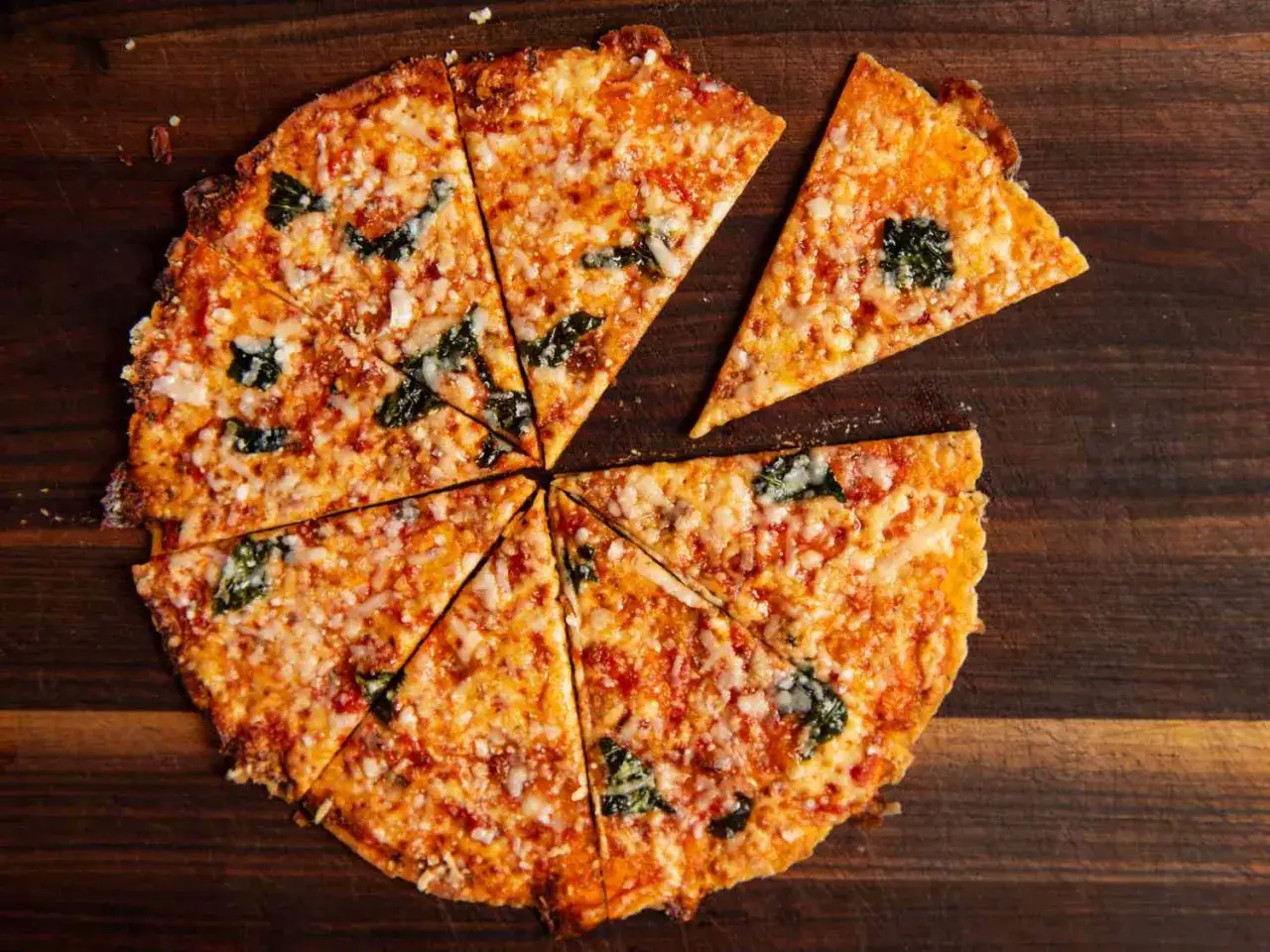 En krispig tortilla pizza med ost och basilika, skuren i bitar p&aring; en tr&auml;sk&auml;rbr&auml;da.