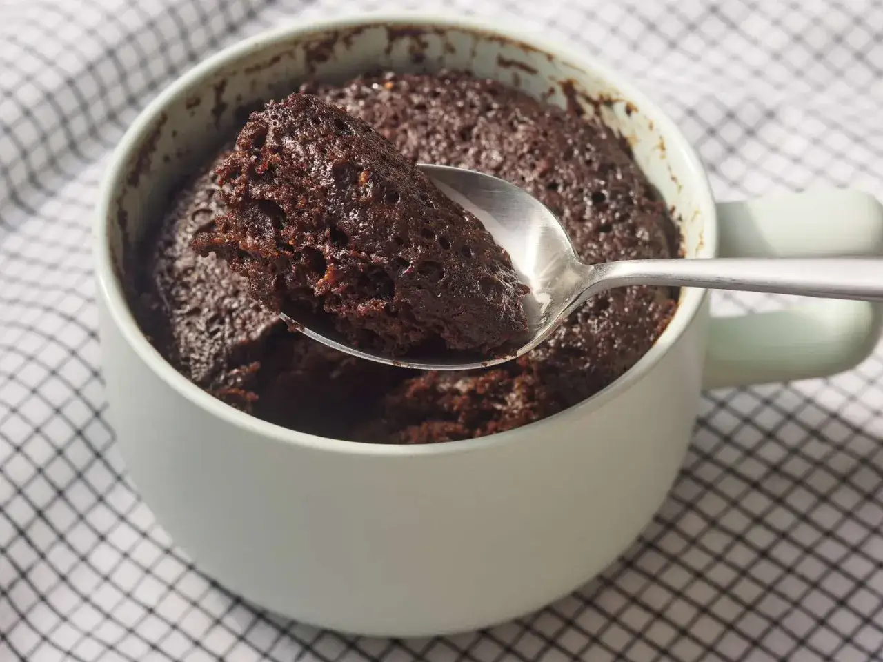 En sked lyfter en bit av en saftig chokladkaka ur en mugg. Perfekt f&ouml;r ett snabbt muggkaka recept.