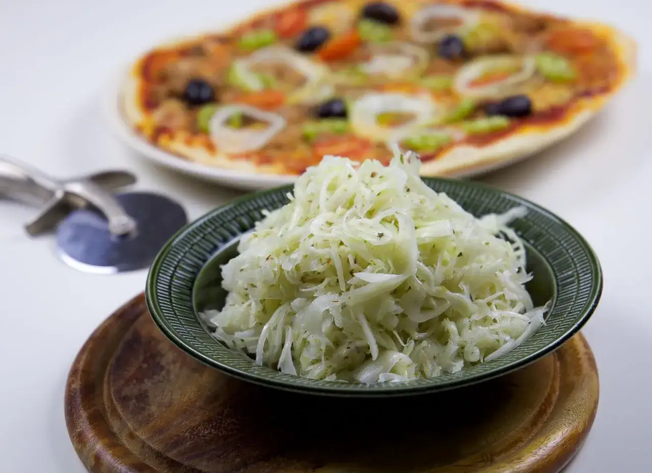 En skål med krispig pizzasallad bredvid en pizza. Perfekt tillbehör för ditt pizzasallad recept.
