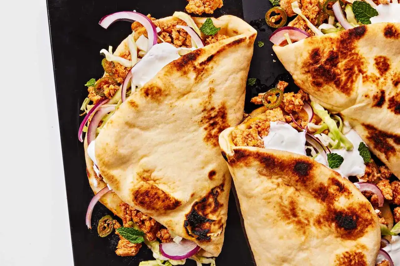 Tre tikka masala-wraps med kyckling, vitlökssås, rödlök och mynta på en svart tallrik.
