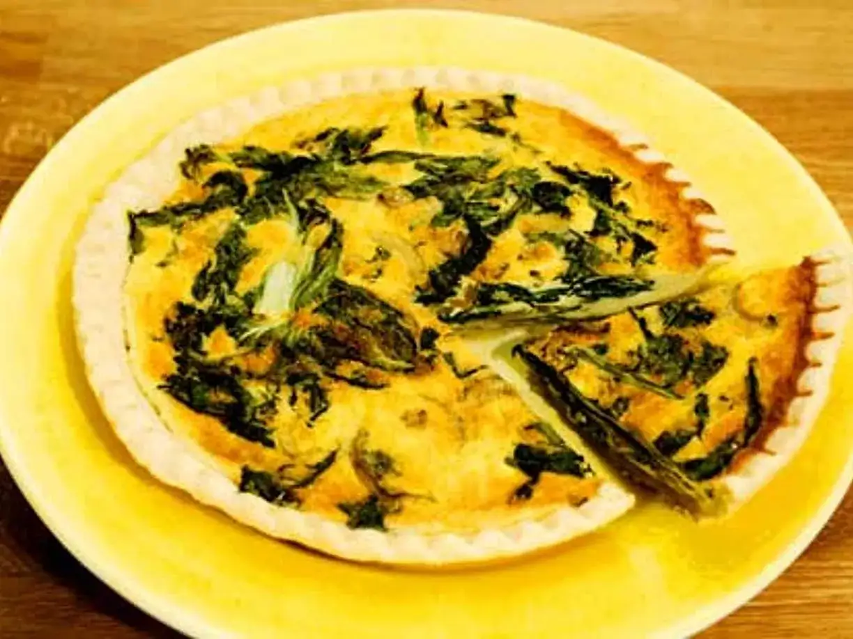 En gyllene, smakrik vegetarisk paj med spenat och &auml;gg, serverad p&aring; en gul tallrik. En bit &auml;r uppskuren.