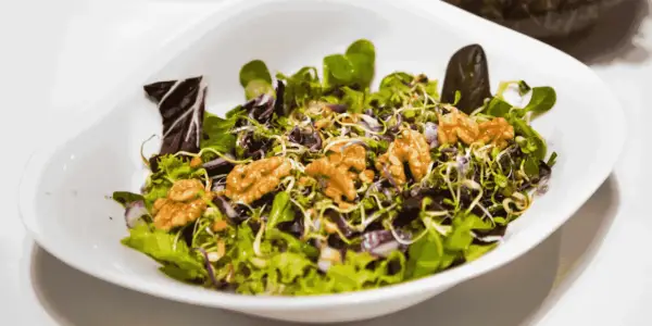 A fresh salad with mixed greens, sprouts, red onion, and walnuts in a white bowl.