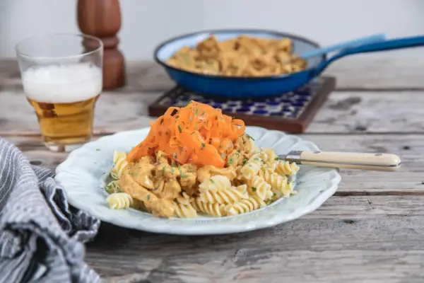En tallrik med rotfrukter och ost och skinksås över pasta. En öl står bredvid.